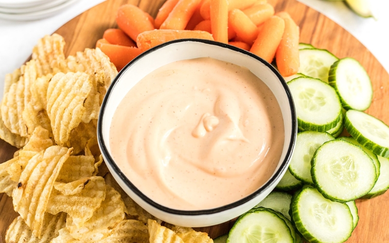 angled shot of sriracha aioli in bowl surrounded by veggies and chips