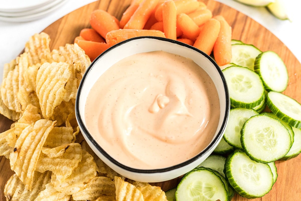 angled shot of sriracha aioli in bowl surrounded by veggies and chips