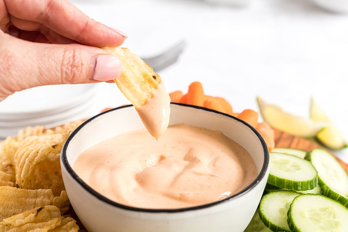 hand holding chip dipping into bowl of spicy aioli