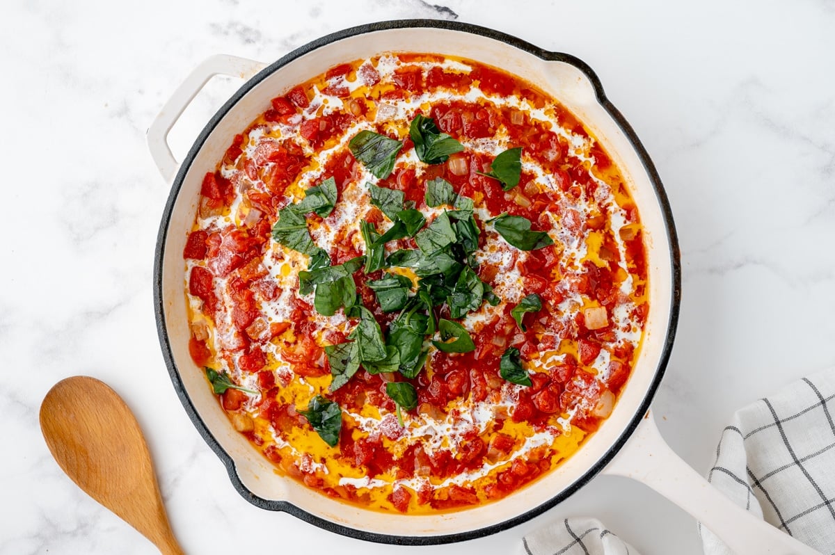 basil and cream added to crushed tomatoes in pan