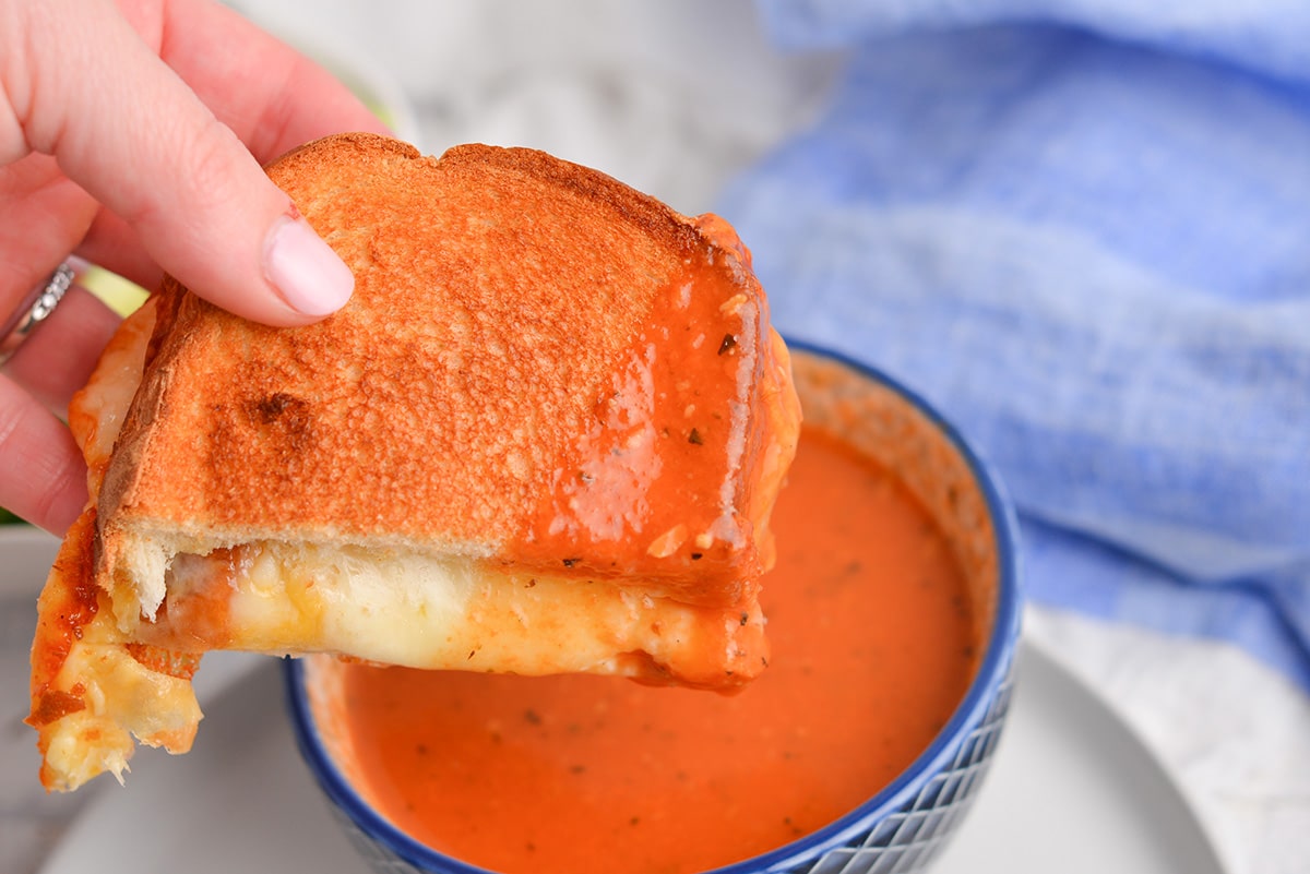 hand dipping air fryer grilled cheese into tomato soup