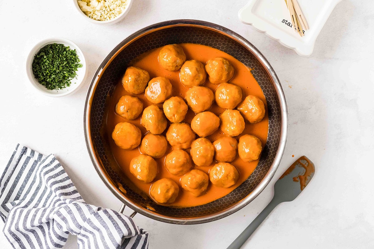 chicken meatballs in a pan topped with buffalo sauce