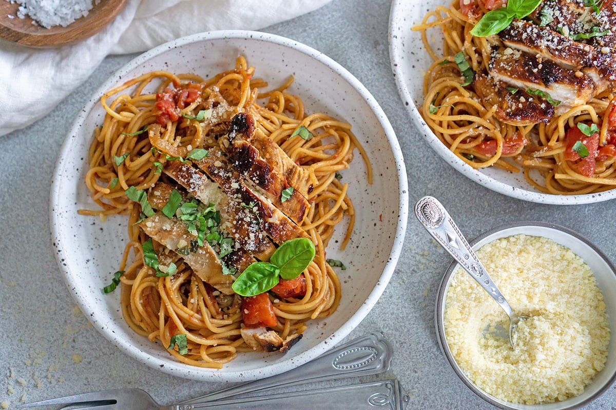 bowl of pasta and chicken next to bowl of parmesan cheese