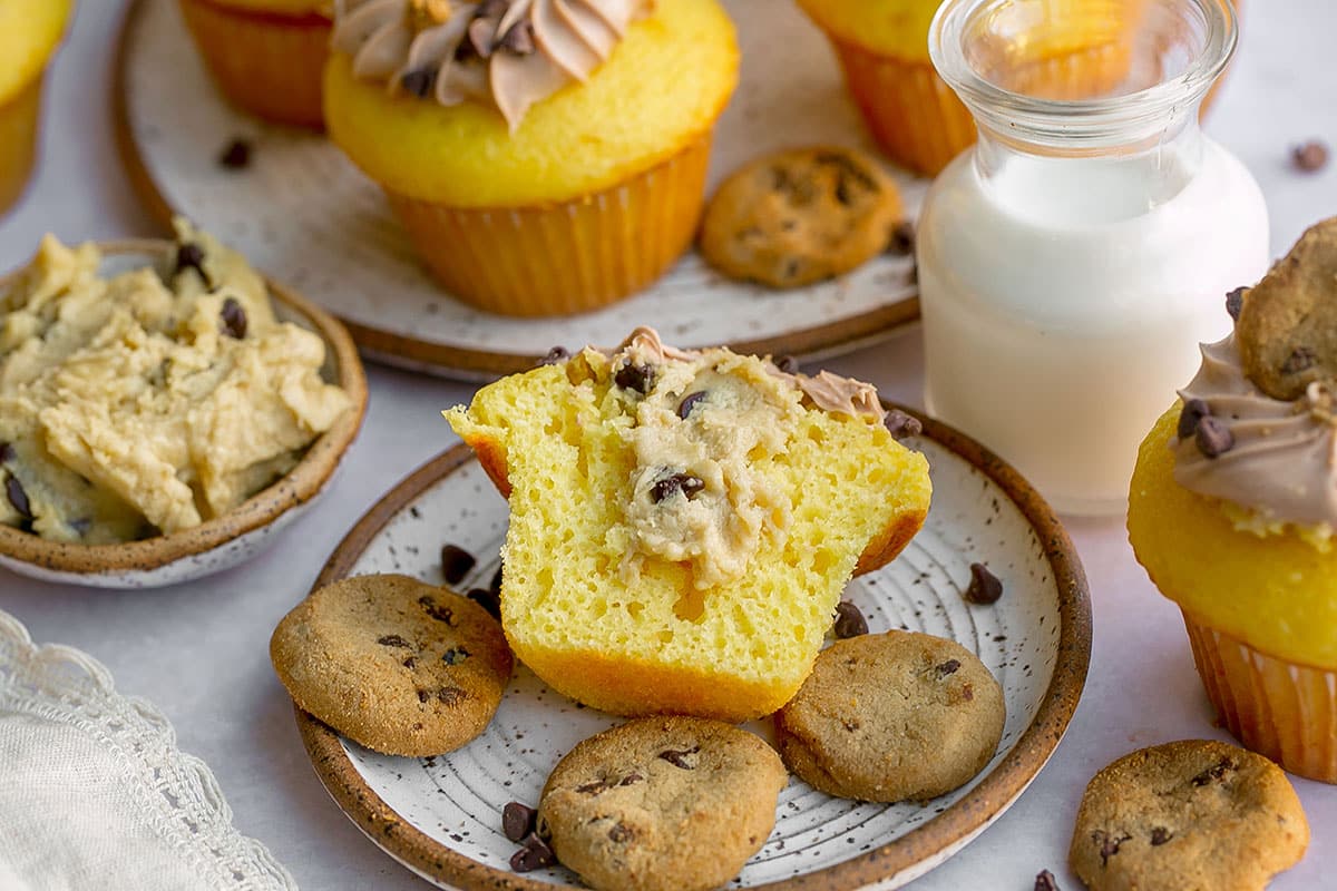 stuffed cookie dough cupcake cut in half on a plate with chocolate chip cookies