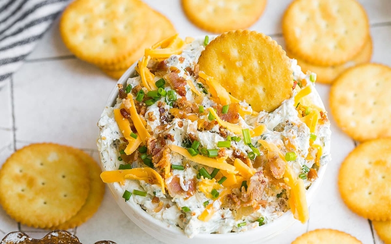 cracker in bowl of cheesy bacon dip