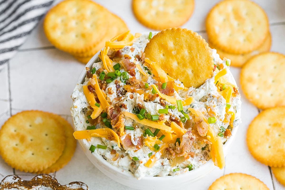 cracker in bowl of cheesy bacon dip