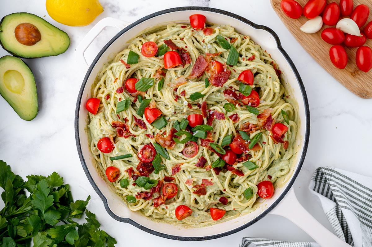 overhead of avocado pasta topped with tomatoes and bacon