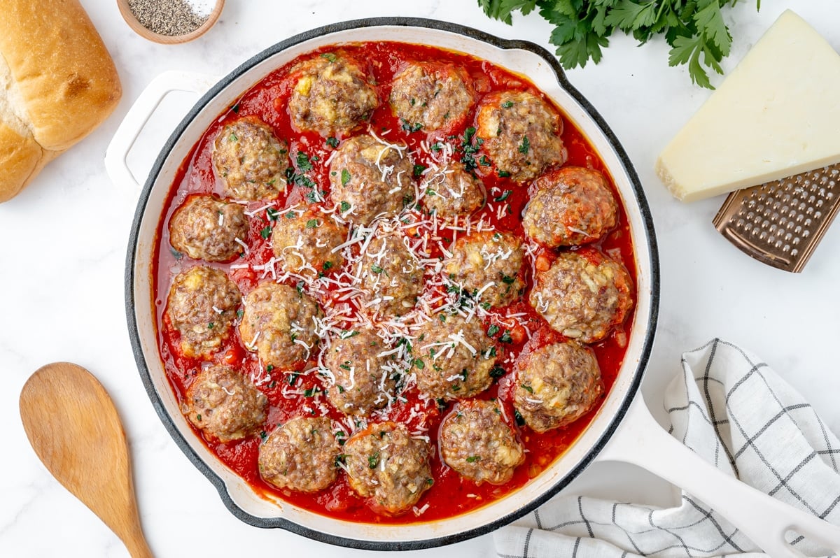 skillet full of meatballs sitting in red sauce with cheese