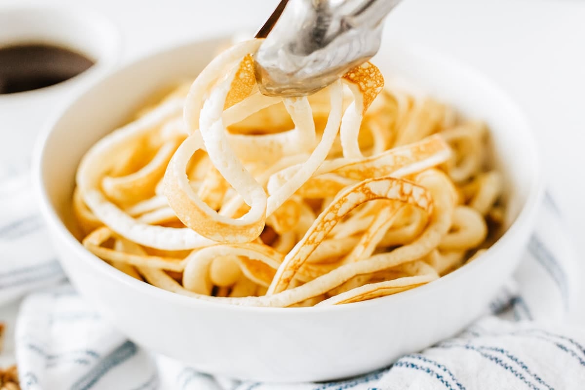 tongs adding pancake spaghetti to bowl