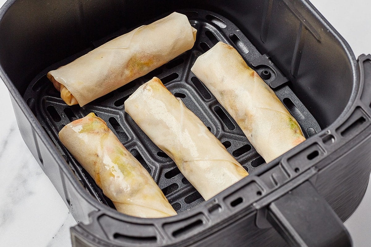 four uncooked vegetable spring rolls in an air fryer basket