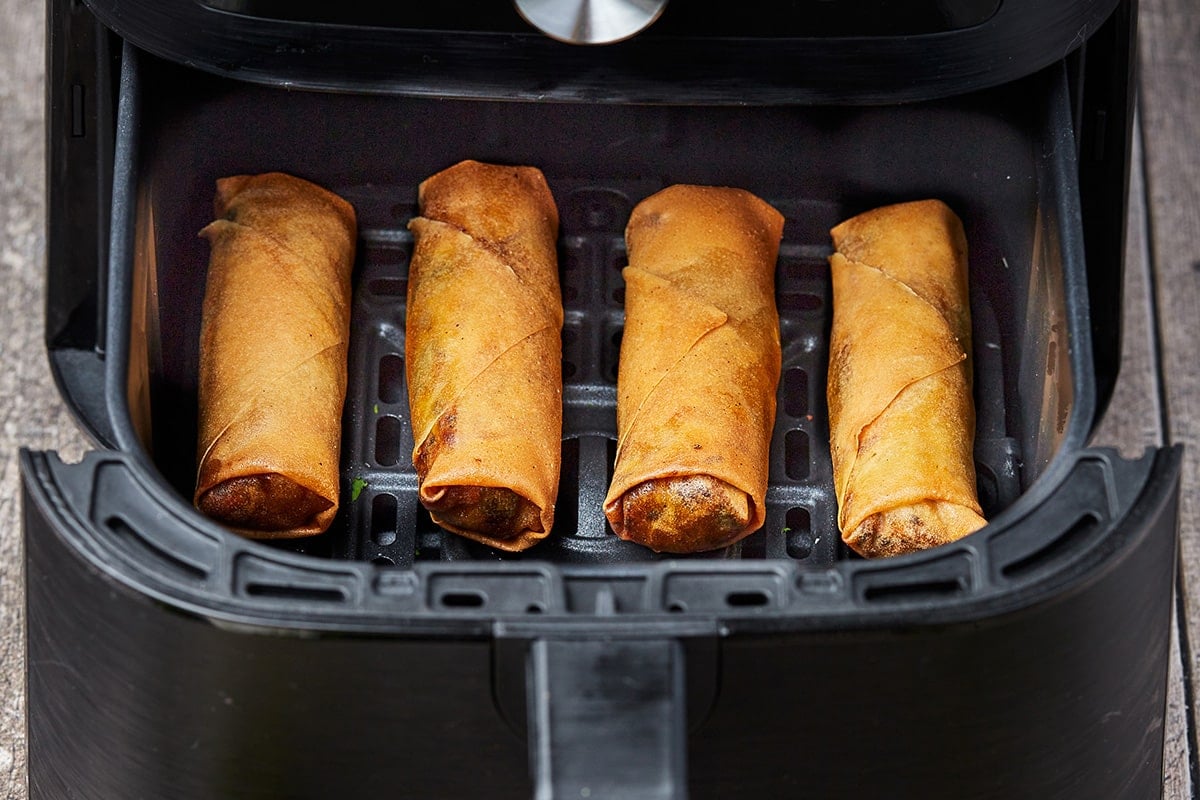 four vegetable spring rolls in an air fryer basket