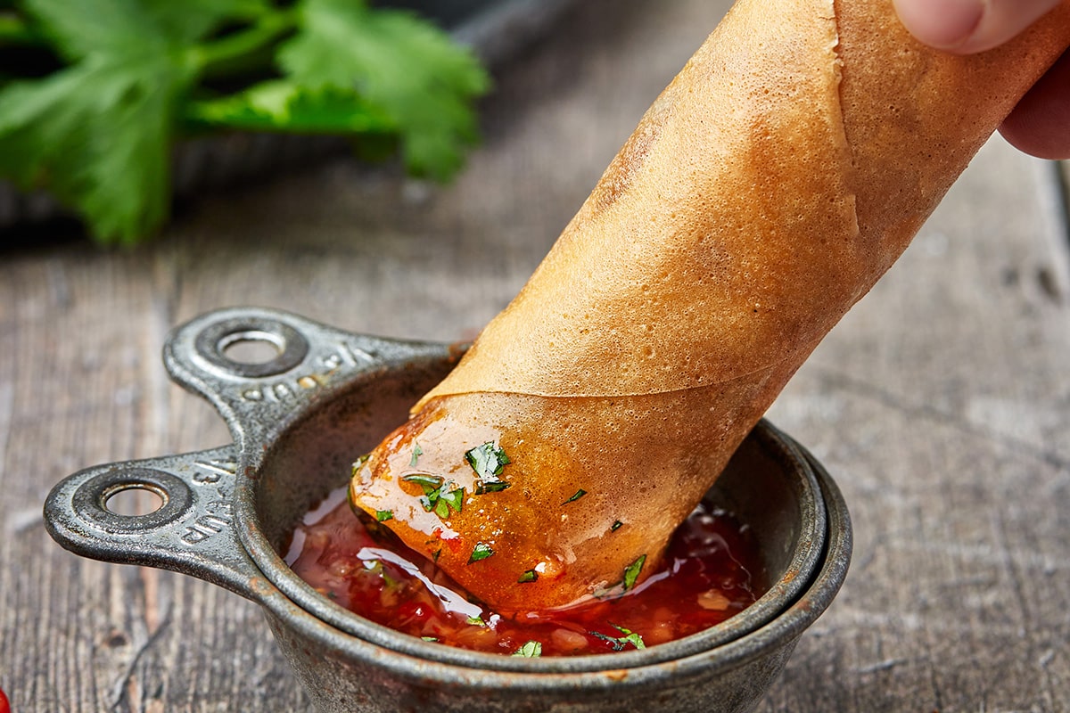 hand dipping spring roll into sauce