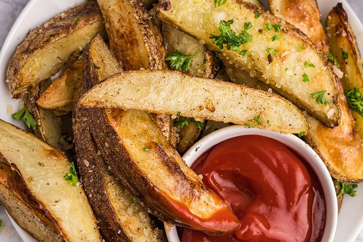 close up of potato wedges on plate with bowl of ketchup