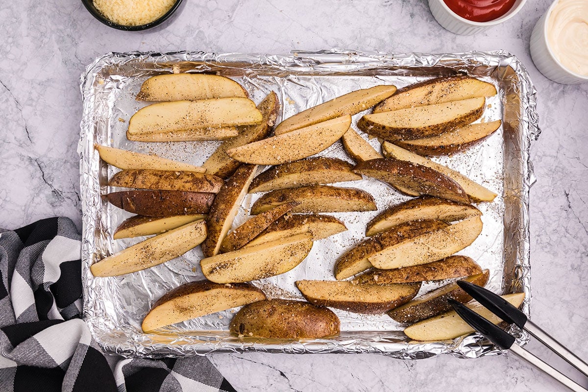 salt and pepper sprinkled onto potato wedges on a baking sheet