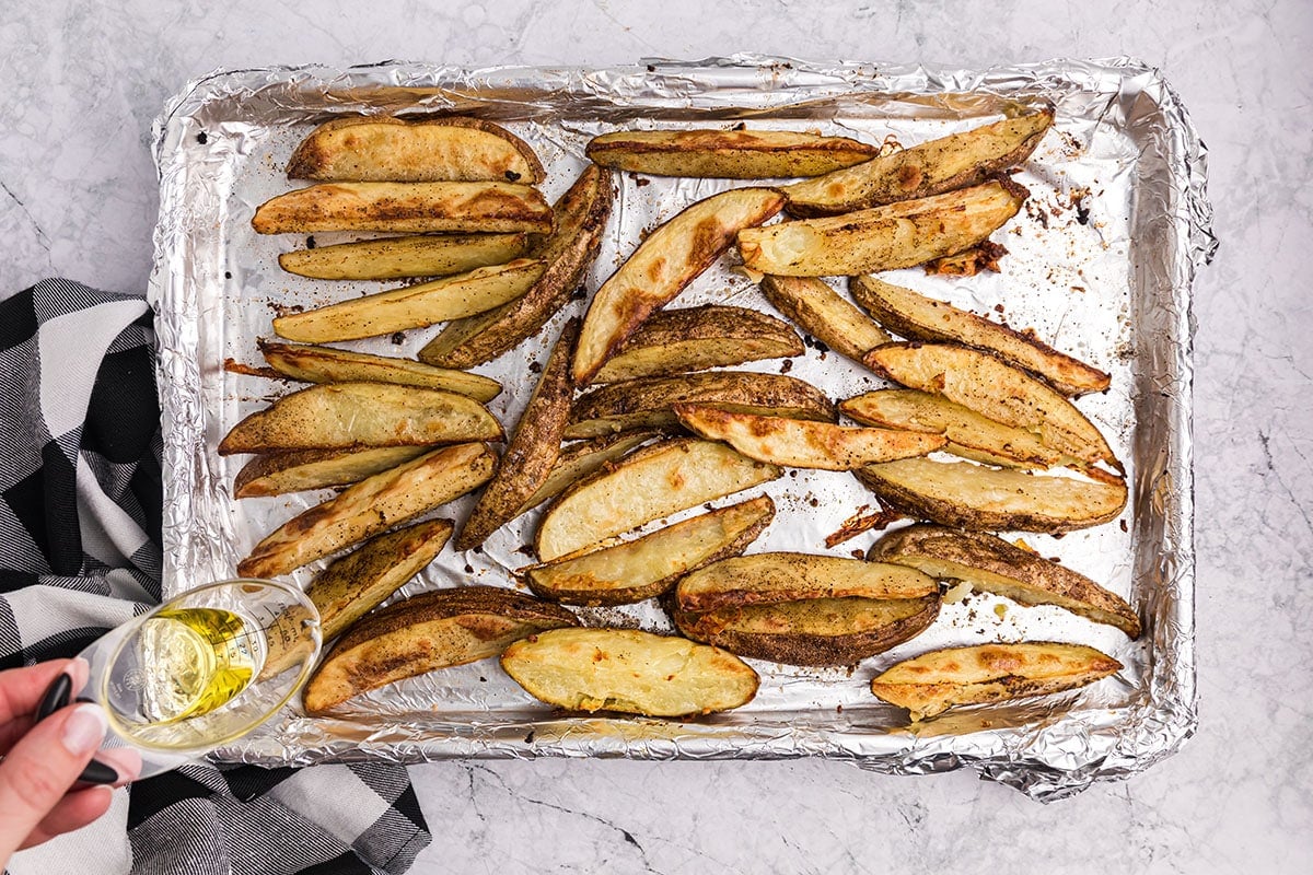 oil poured onto baked potato wedges on a baking sheet