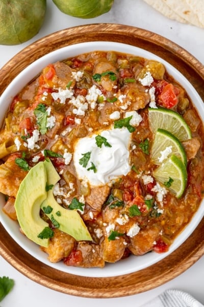 bowl of chili verde topped with sour cream, lime and avocado