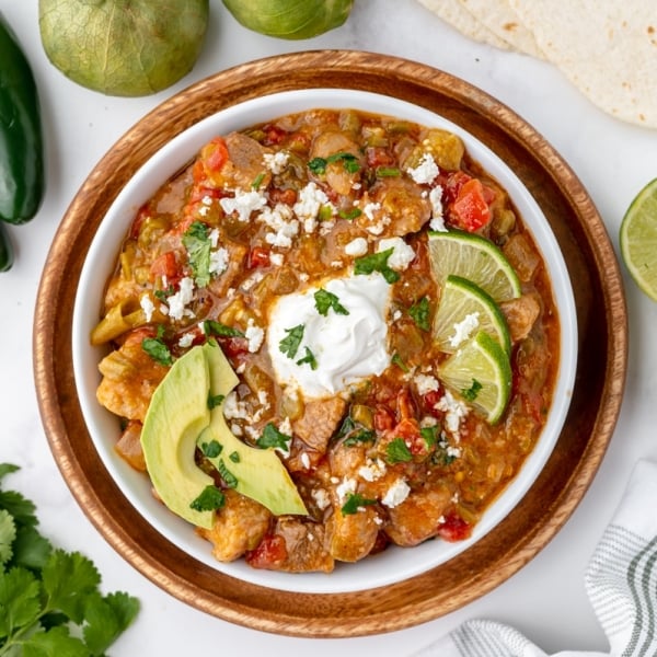 bowl of chili verde topped with sour cream, lime and avocado