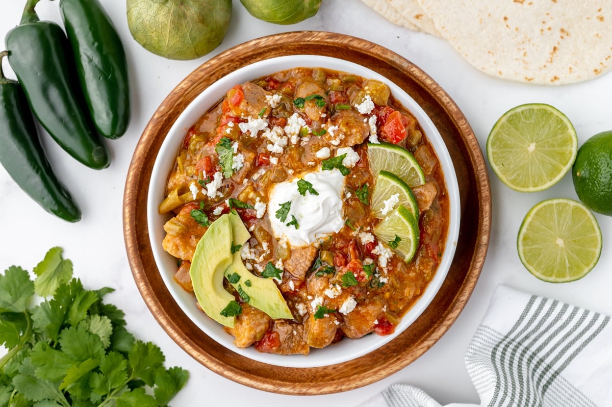 bowl of chili verde topped with sour cream, lime and avocado