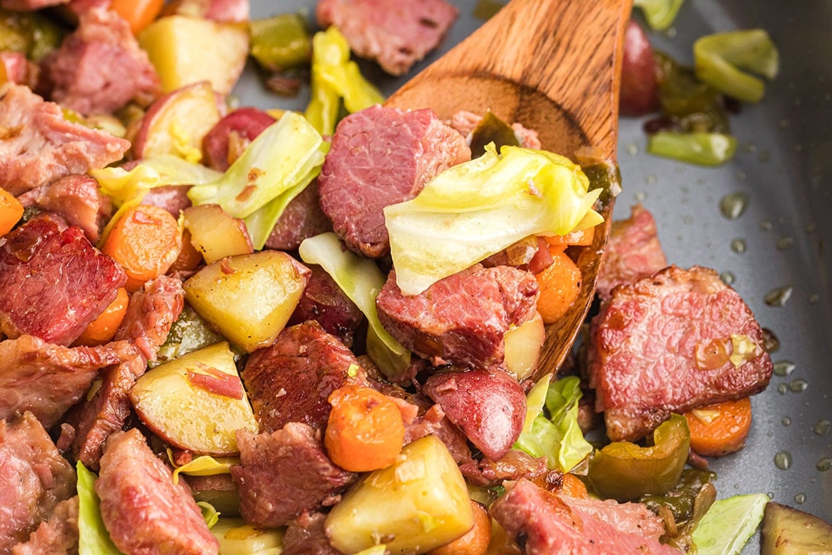 angled shot of corned beef hash in pan with wooden spoon