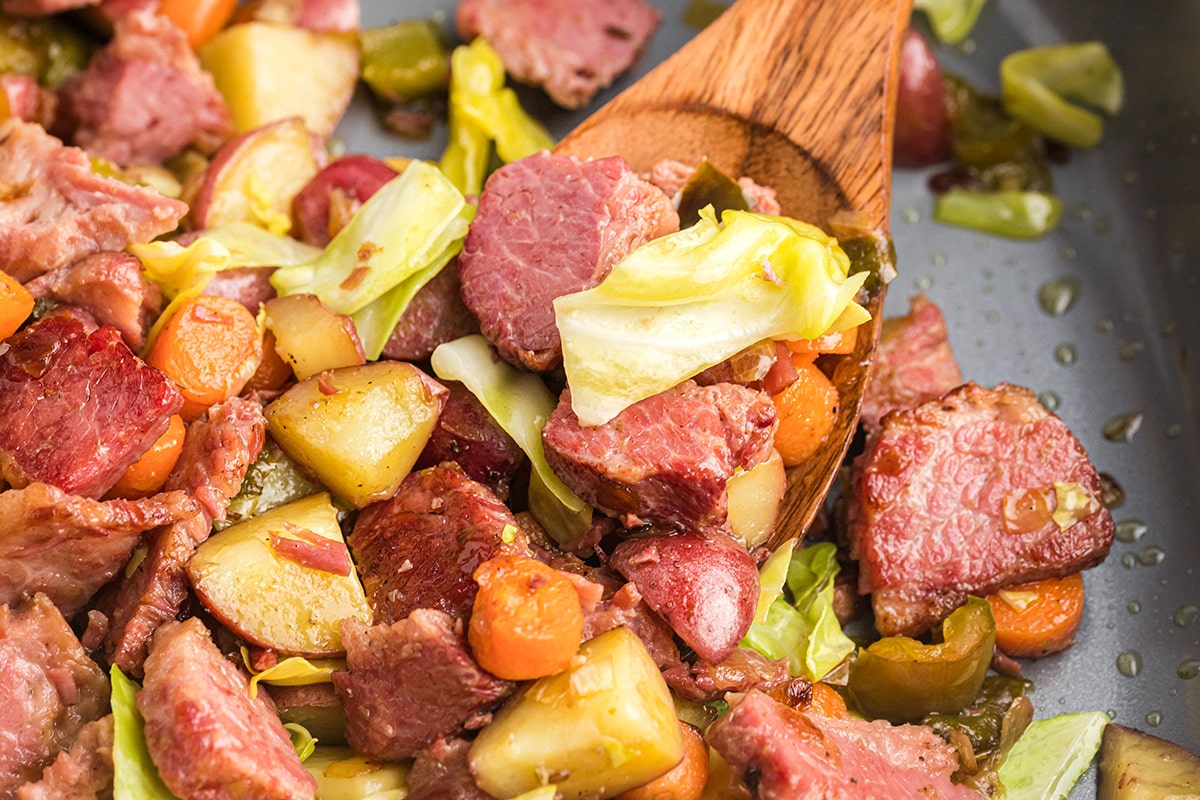 angled shot of corned beef hash in pan with wooden spoon