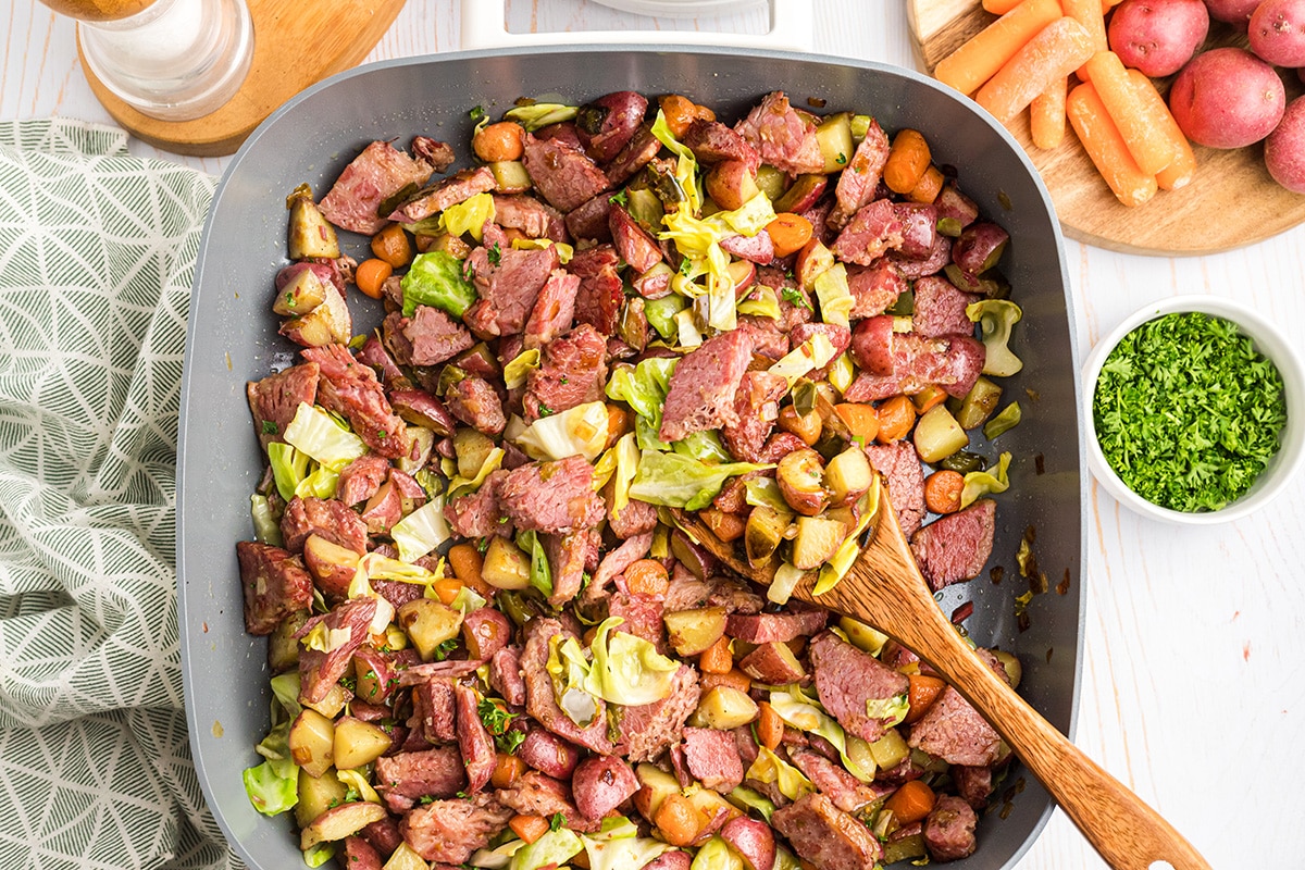 corned beef hash in a skillet with a wooden spoon