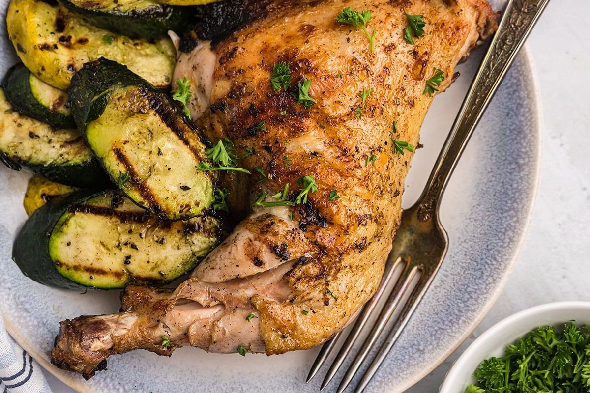 close up of chicken leg on plate with fork and zucchini