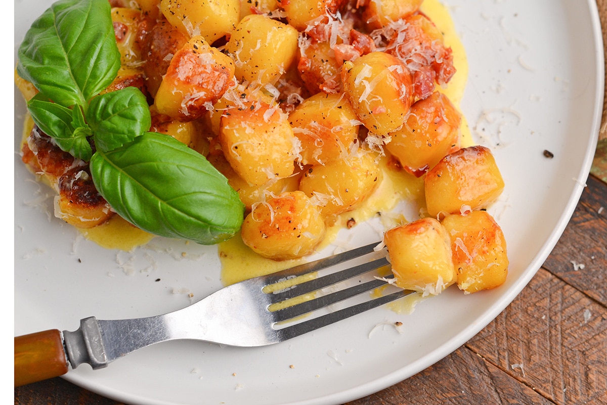 angled shot of fork on plate of gnocchi carbonara