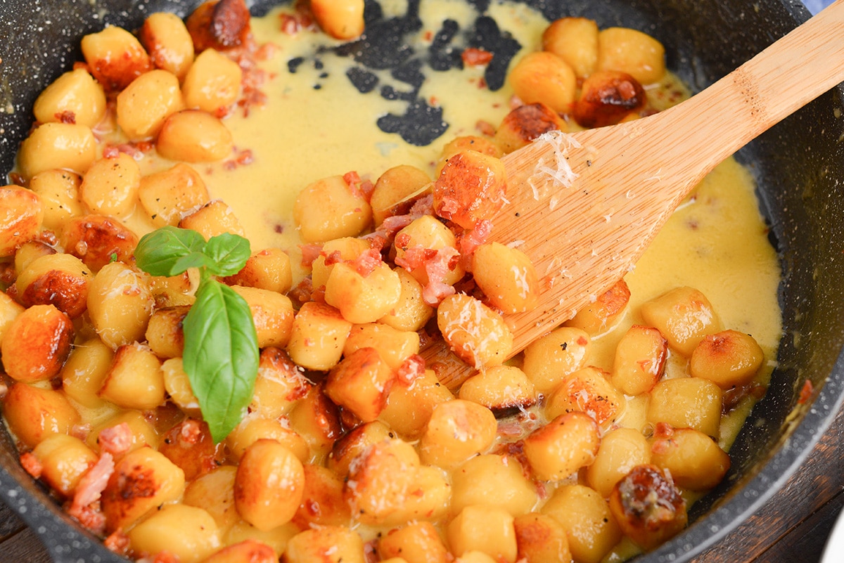 gnocchi carbonara in a pan with a wooden spoon