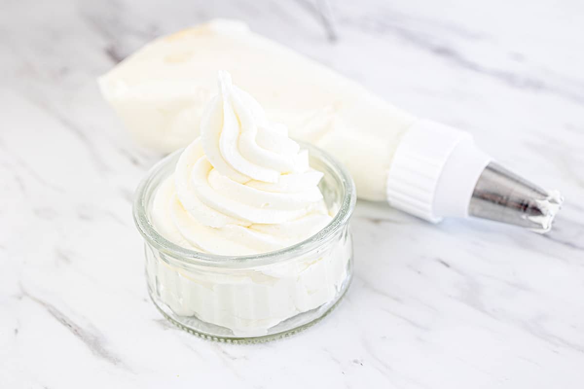 vanilla buttercream frosting in a glass bowl with bag of frosting behind it