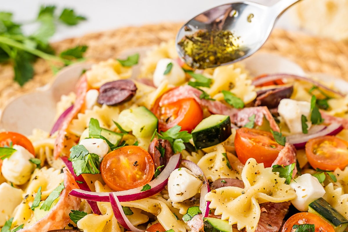 spoon pouring dressing onto antipasto pasta salad