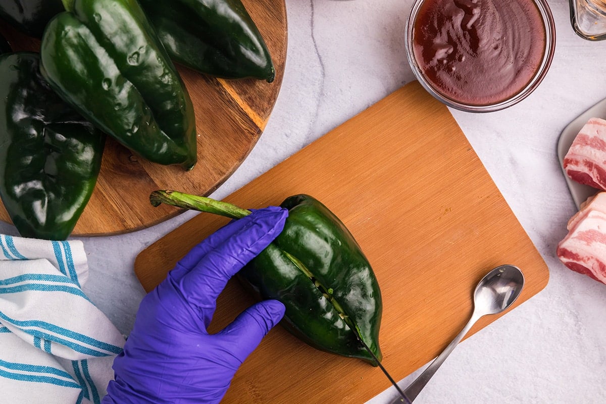 hand holding poblano pepper and cutting on a knife