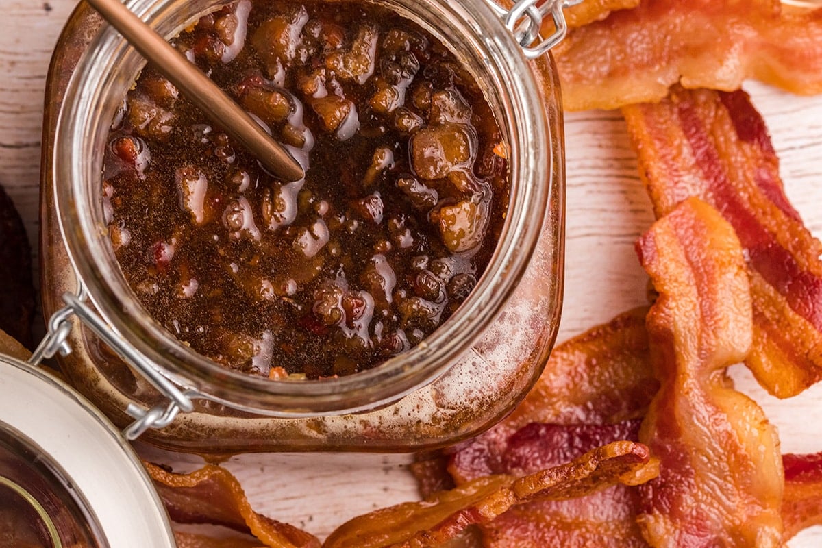overhead shot of jar of bacon jam with spoon in it and bacon next to it