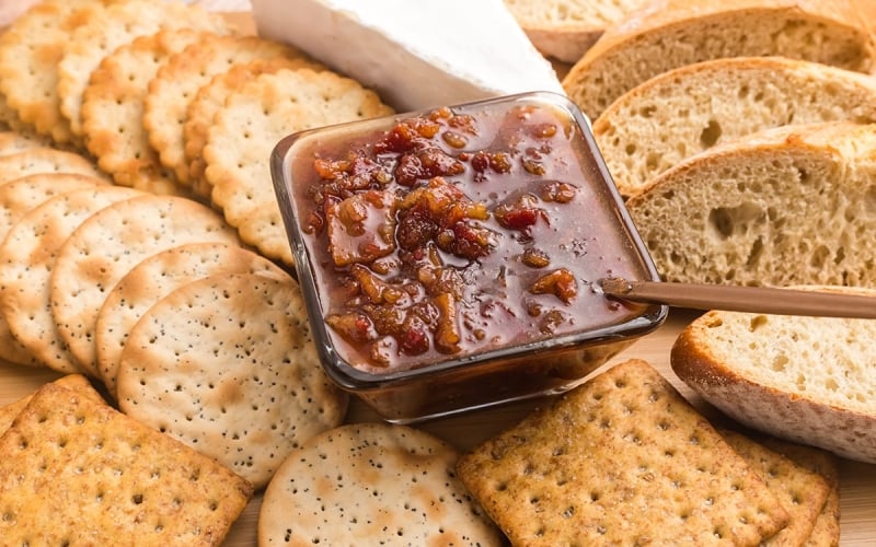 angled shot of bowl of bacon jam on board with breads
