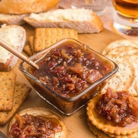 angled shot of bowl of bacon jam with spoon in it on board with crackers