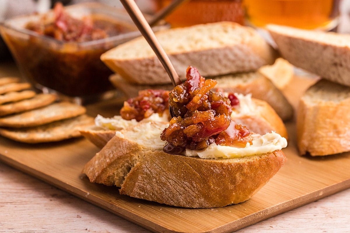 spoon adding bacon jam to bread with cheese