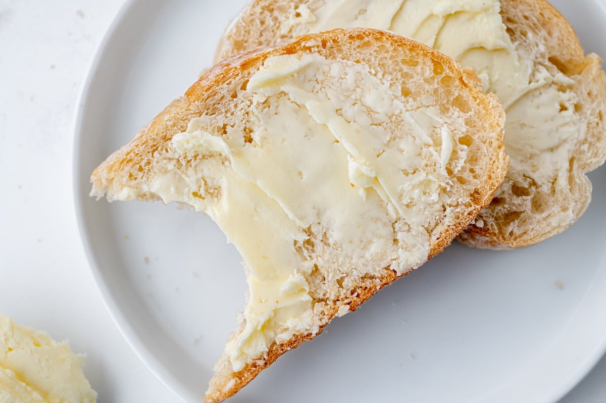 close up overhead shot of bite taken out of bread slathered with homemade butter