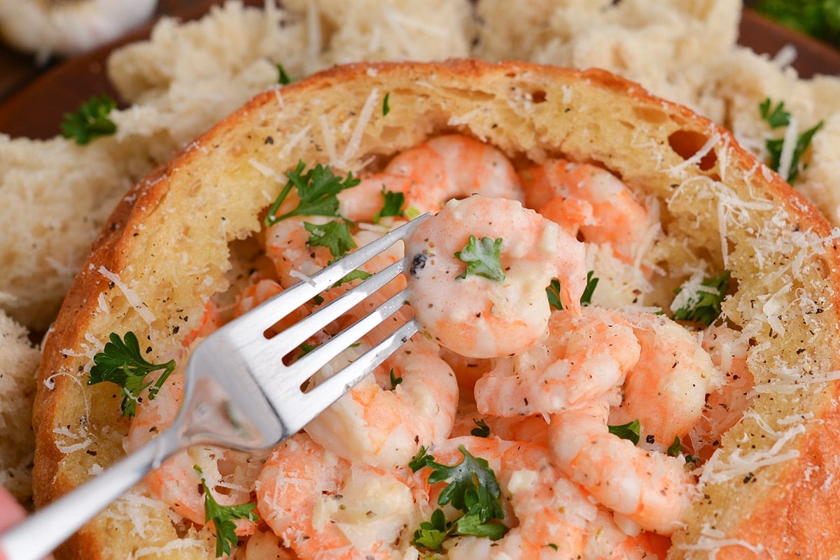 fork holding a curled pink shrimp in cream sauce