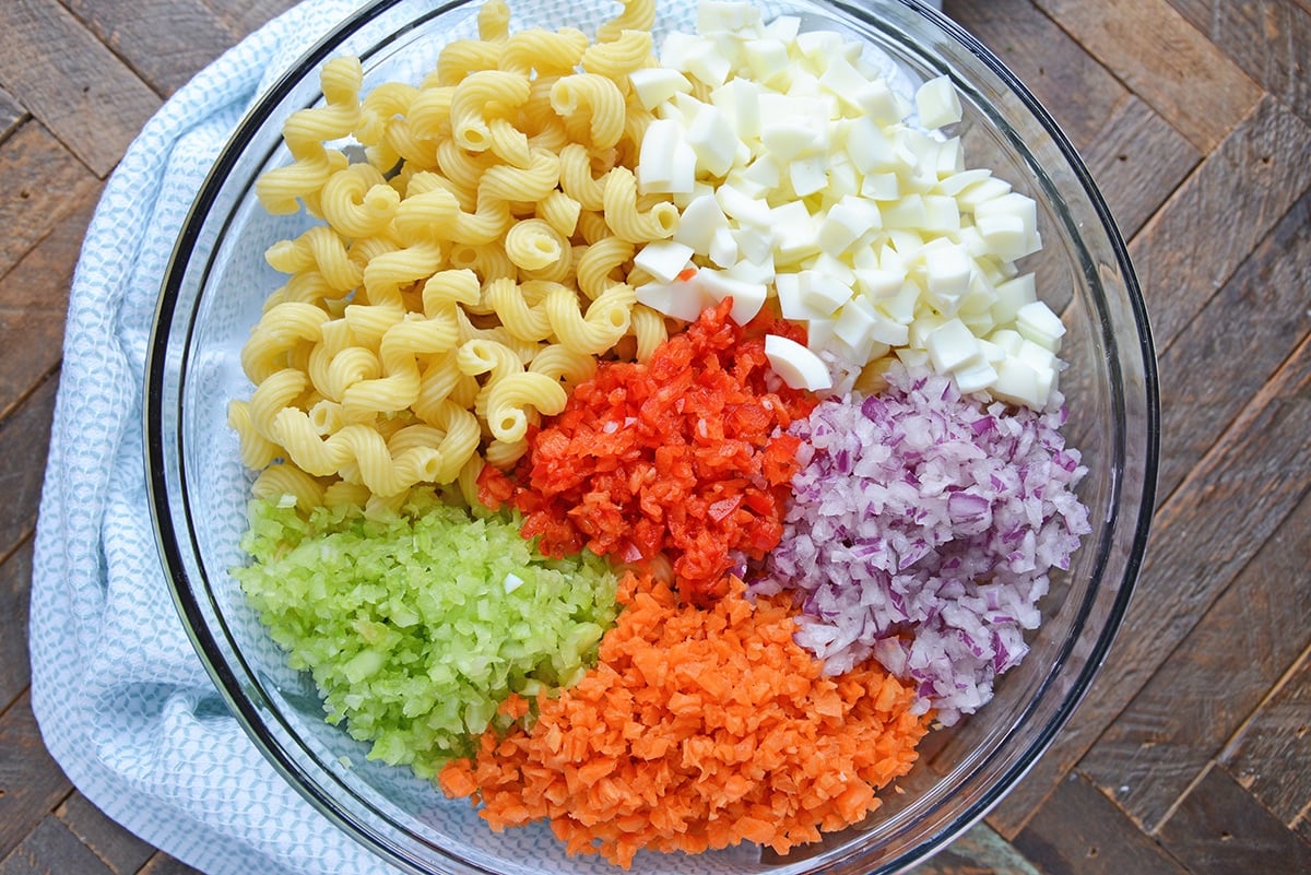 ingredients for deviled egg macaroni salad in a large glass mixing bowl