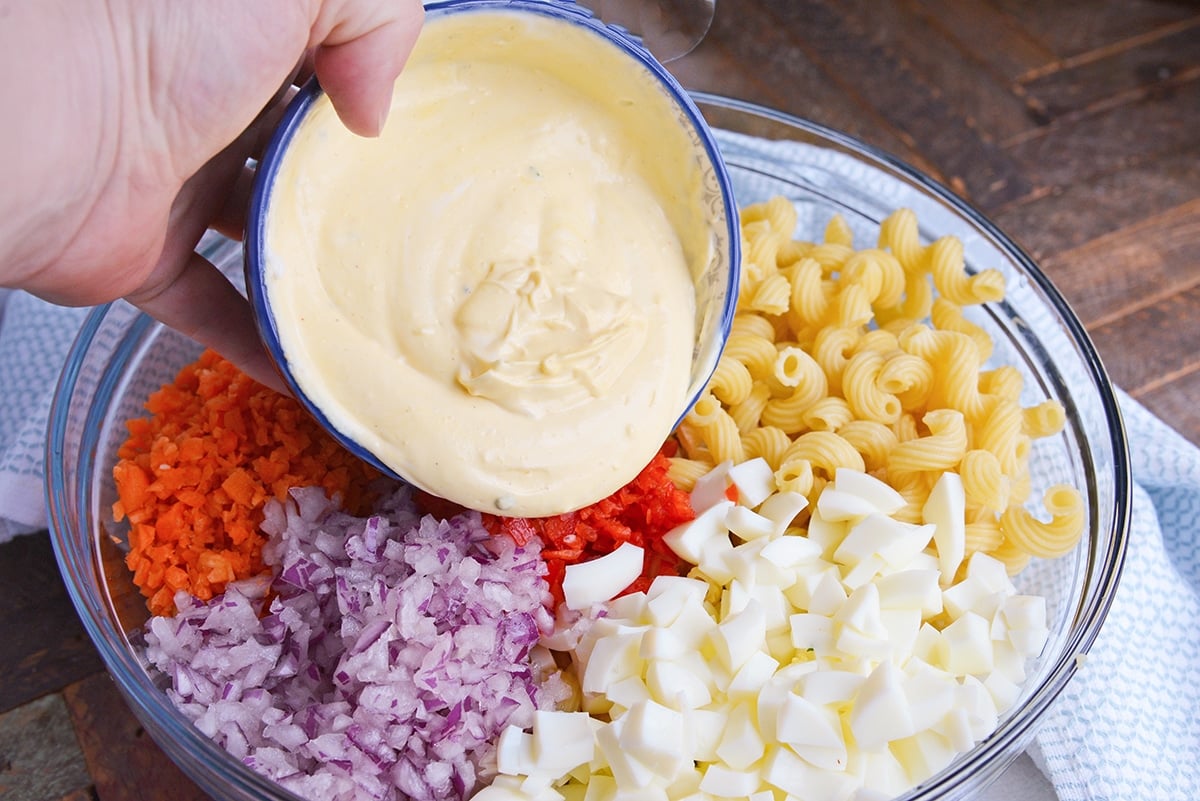 pouring creamy deviled egg filling over mac salad ingredients