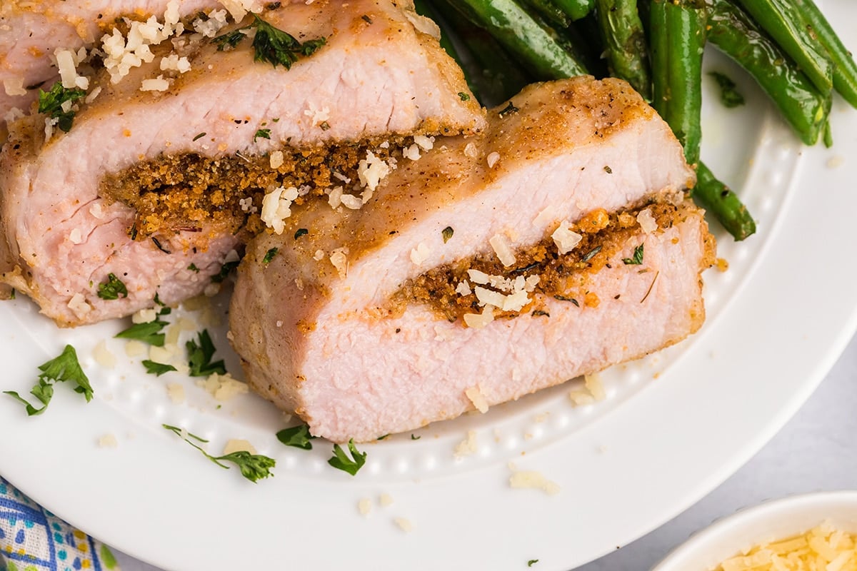 angled shot of sliced grilled pork chop on plate with green beans