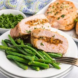 two halves of a grilled stuffed pork chop on a plate with green beans