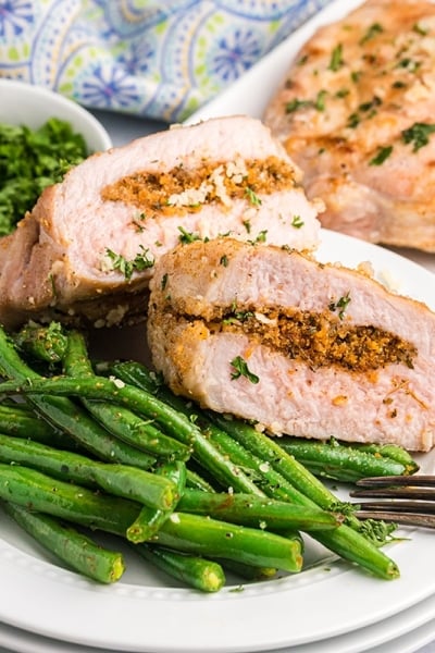 two halves of a grilled stuffed pork chop on a plate with green beans