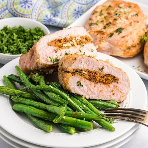 two halves of a grilled stuffed pork chop on a plate with green beans