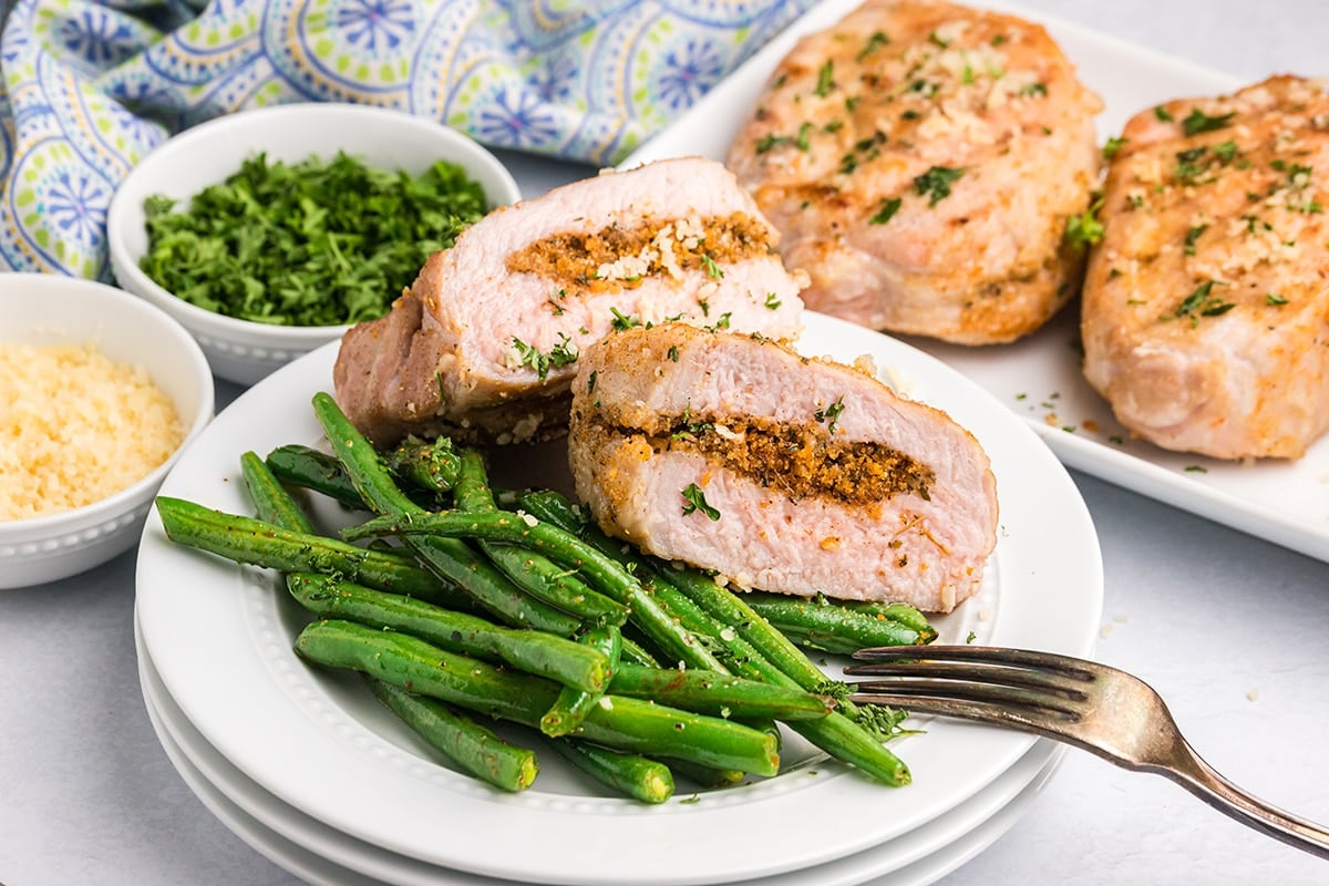 two halves of a grilled stuffed pork chop on a plate with green beans