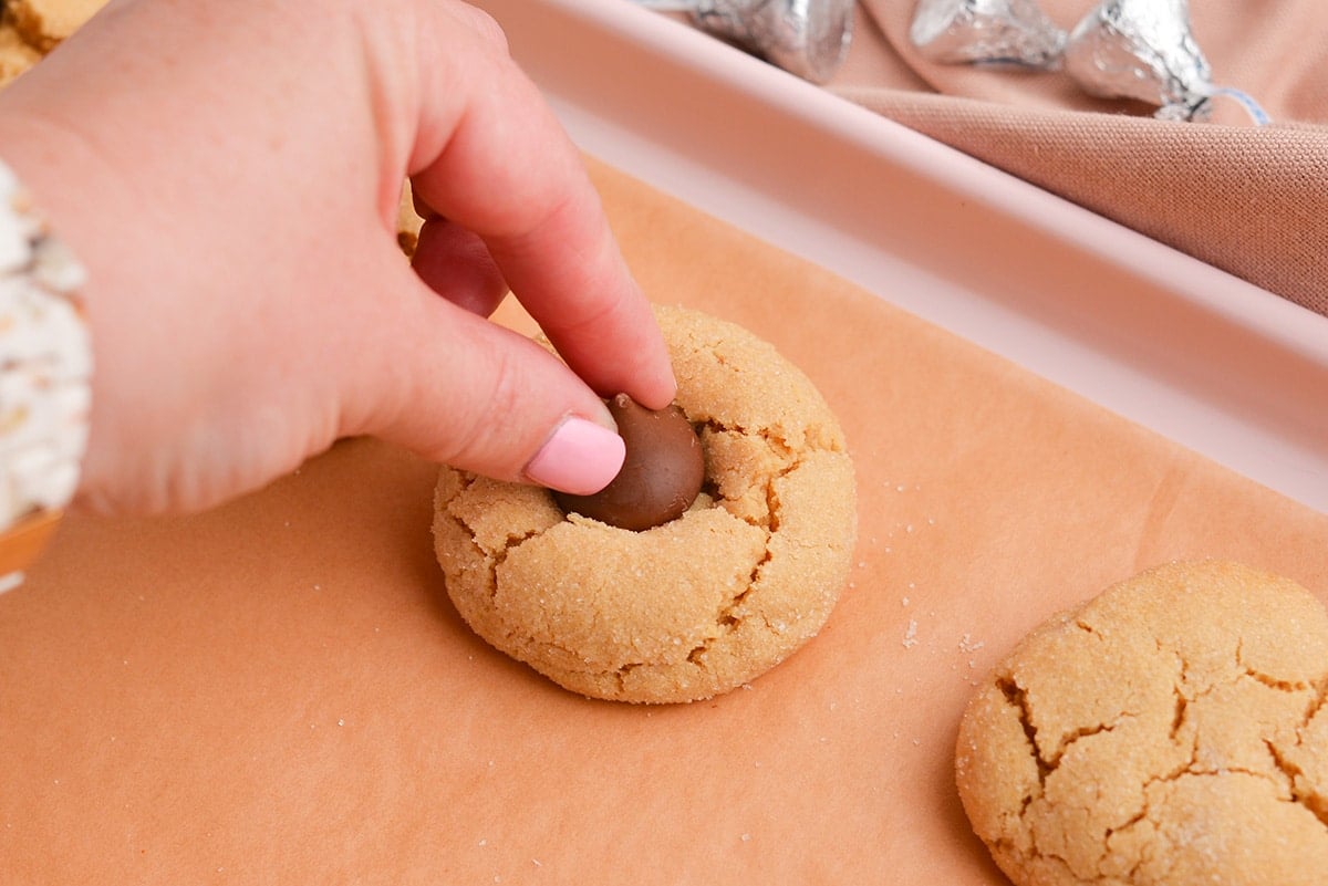 hand adding chocolate kiss to peanut butter cookie