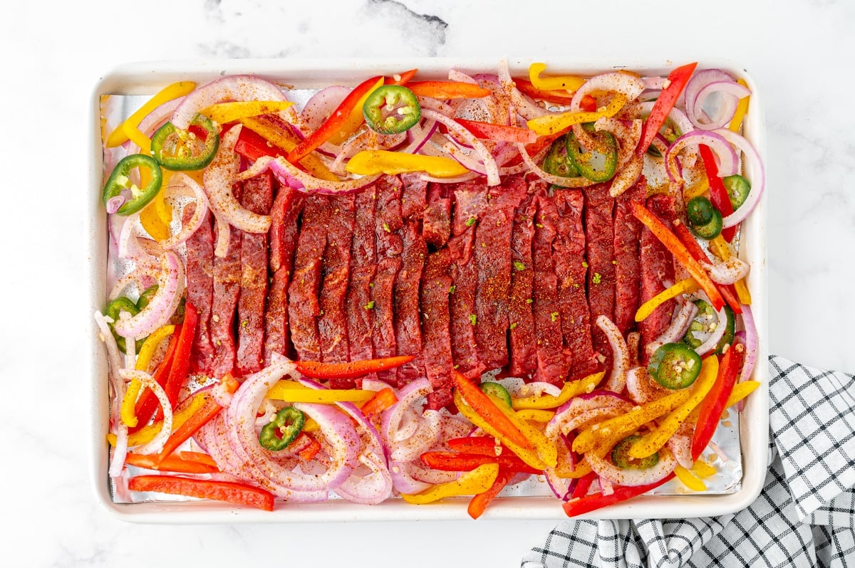 overhead shot of raw steak fajitas on a sheet pan