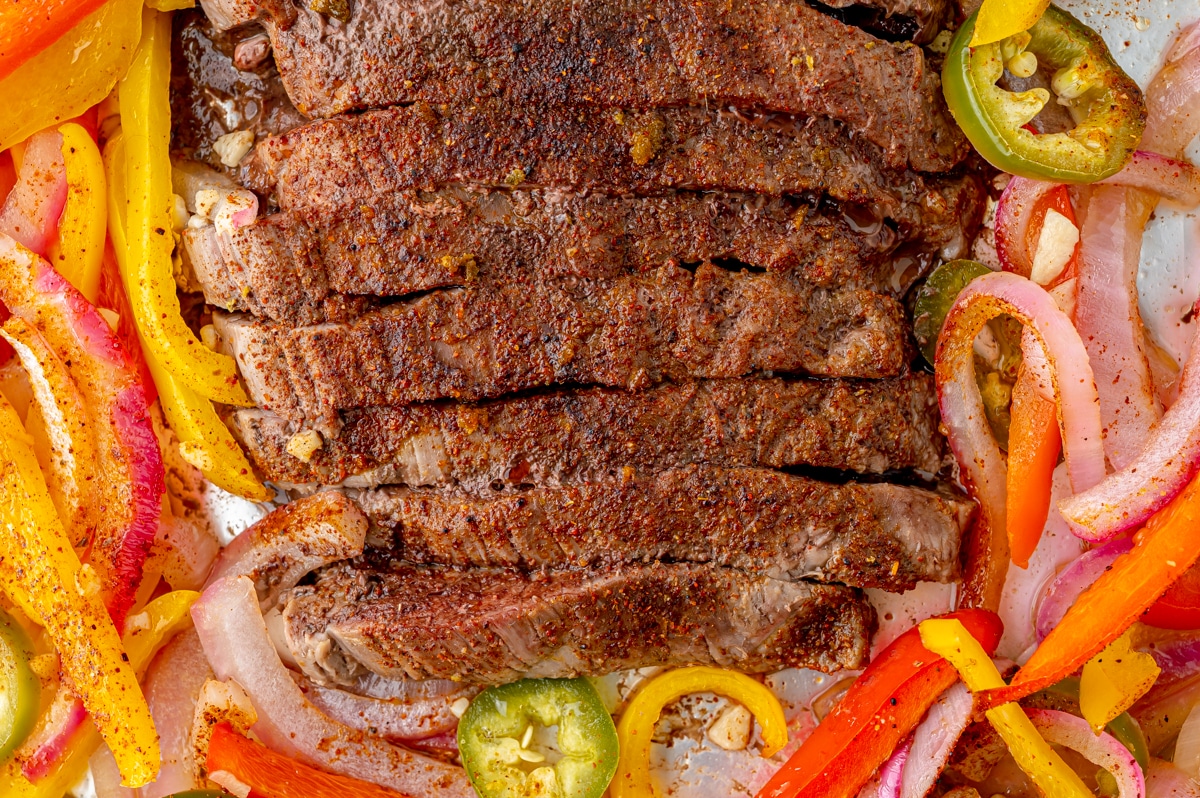 close up of steak fajitas on a sheet pan with cooked veggies