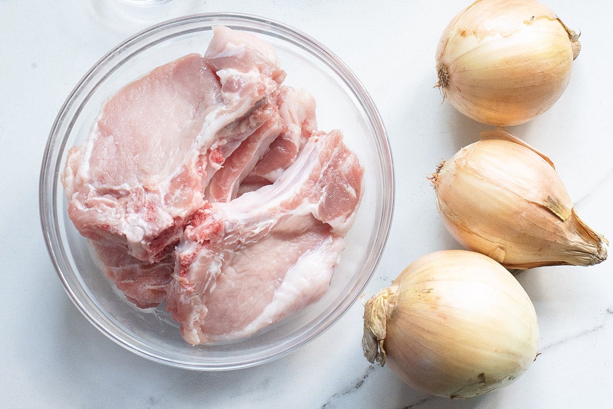 raw pork chops in a bowl next to three onions