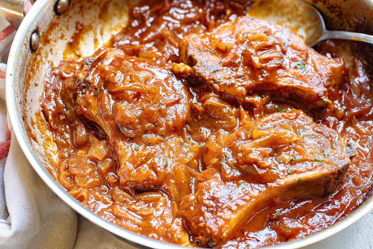 angled shot of smothered pork chops in pan