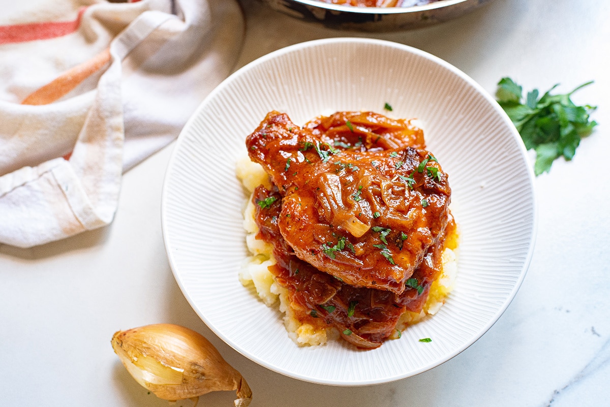 overhead shot of smothered pork chop on a plate over mashed potatoes